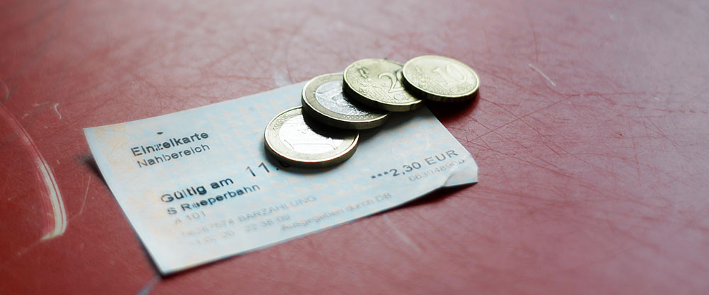 Symbolbild einer HVV-Fahrkarte "Nahbereich". Darauf liegen 2,30 Euro in bar. / Symbol photo of a HVV "local journey" ticket. On top there's 2.30 Euro in cash.